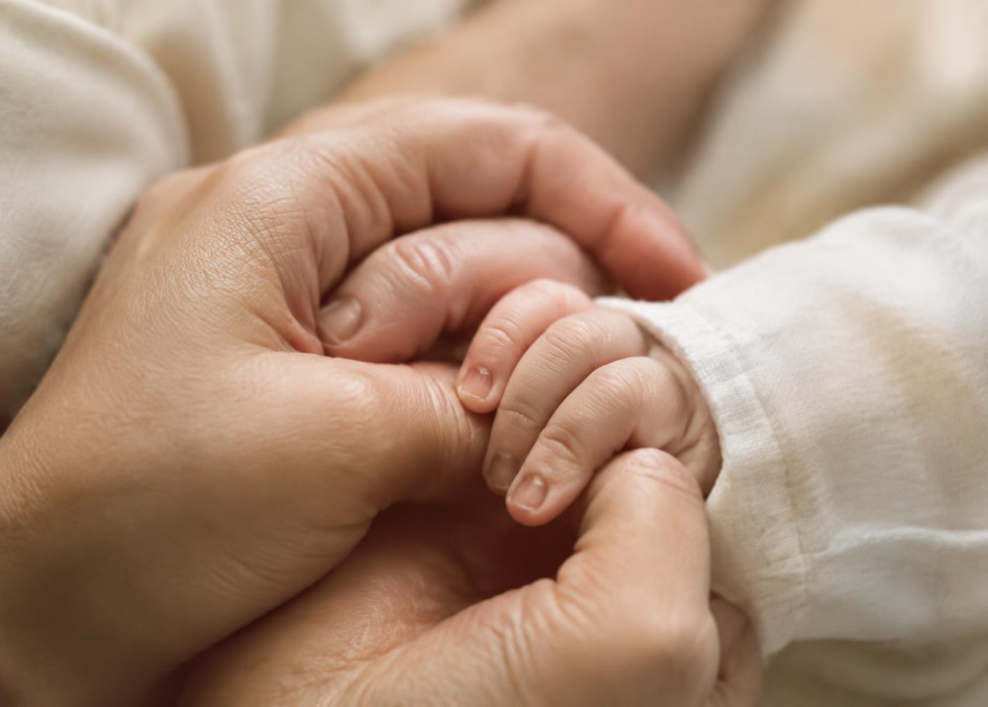 A mother's hands gently holding her newborn's hand